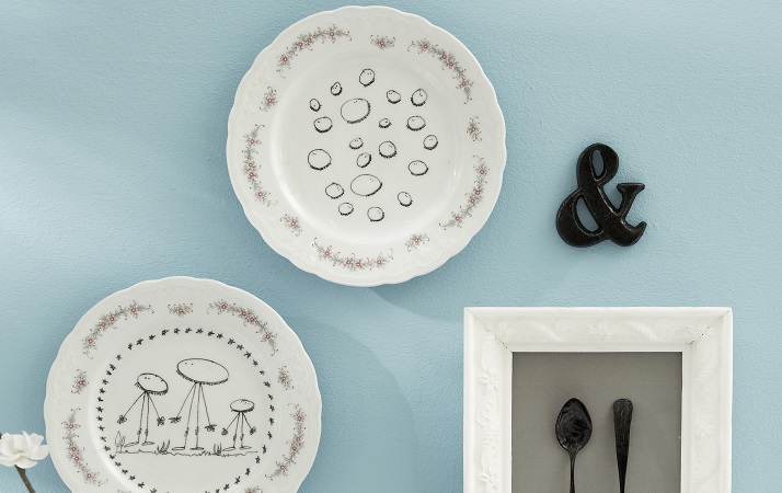 Wall decoration for the kitchen with painted plates and framed black spoons behind glass